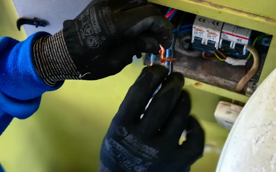 Manos con guantes preparando y conectando conductores dentro de un tablero